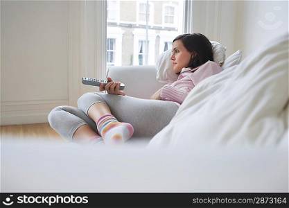 Woman lying on sofa watching television
