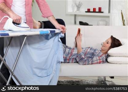 Woman lying on the couch reading while her boyfriend does the housework