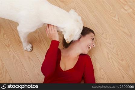 Woman lying on the floor and her dog licking her face