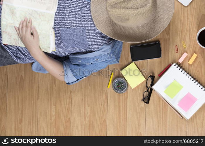 woman lying on wooden floor with hat, mobile phone, notebook and map