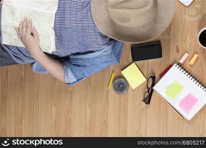 woman lying on wooden floor with hat, mobile phone, notebook and map