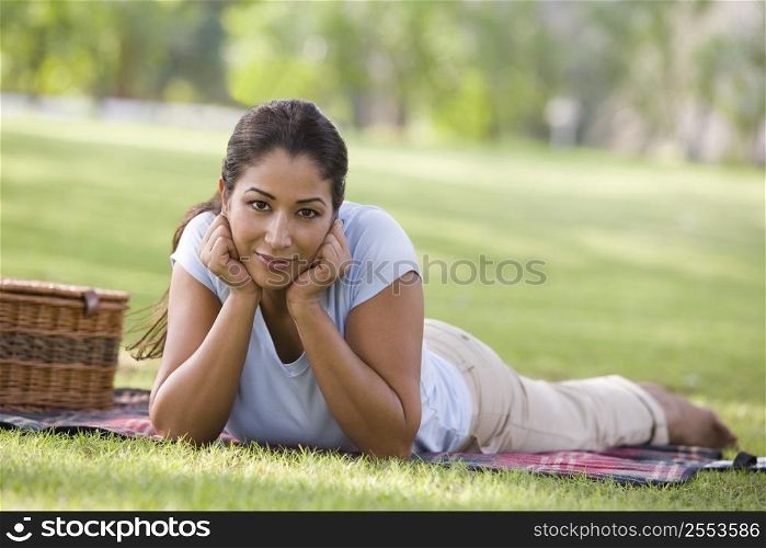 Woman lying outdoors at park with picnic basket smiling (selective focus)