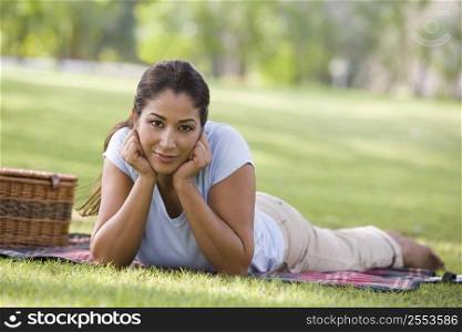 Woman lying outdoors at park with picnic basket smiling (selective focus)