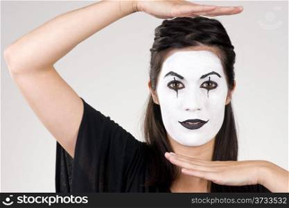 Woman made up in white face frames her features with her hands