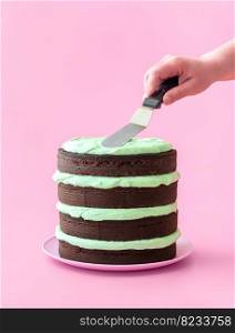 Woman makes a mint chocolate cake, minimalist on a pink background. Delicious homemade layered cake, with dark chocolate and mint-flavored buttercream