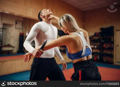 Woman makes punch to the throat, self-defense workout with male personal trainer, gym interior on background. Female person on training, self defense practice. Woman makes punch to the throat, self-defense
