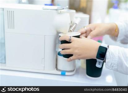 Woman making a cup of hot coffee with capsule coffee machine. Woman holding black cup taking coffee from a capsule coffee machine on the table. Espresso maker. Morning drink. Modern home equipment.