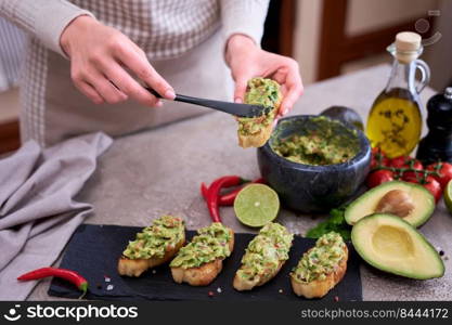woman making bruschetta with freshly made guacamole on domestic kitchen.. woman making bruschetta with freshly made guacamole on domestic kitchen