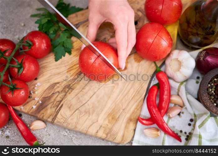 woman making notch on a tomato on wooden cutting board on grey kitchen concrete or stone table.. woman making notch on a tomato on wooden cutting board on grey kitchen concrete or stone table