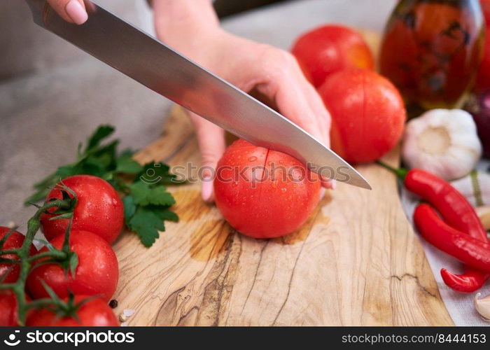 woman making notch on a tomato on wooden cutting board on grey kitchen concrete or stone table.. woman making notch on a tomato on wooden cutting board on grey kitchen concrete or stone table