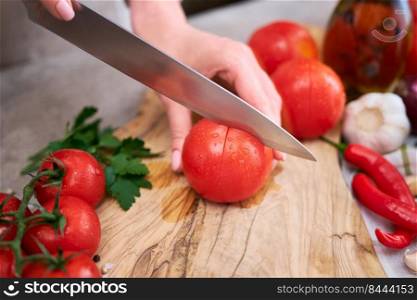 woman making notch on a tomato on wooden cutting board on grey kitchen concrete or stone table.. woman making notch on a tomato on wooden cutting board on grey kitchen concrete or stone table
