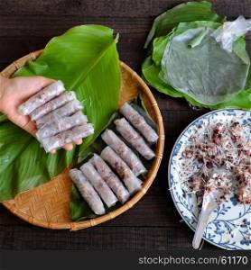 Woman making spring rolls or cha gio at home, homemade food stuffing from meat and wrapper by rice paper, hand rolling Vietnamese egg roll on green leaf background