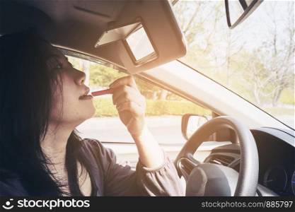Woman making up her face using lipstick while driving car, unsafe behavior
