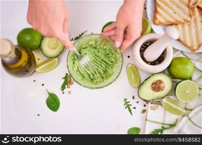 Woman mashing avocados in a glass bowl with a fork to prepare toasts.. Woman mashing avocados in a glass bowl with a fork to prepare toasts