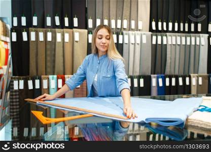 Woman measures the fabric in textile store. Shelf with cloth for sewing on background, clothing patterns choice in shop. Woman measures the fabric in textile store