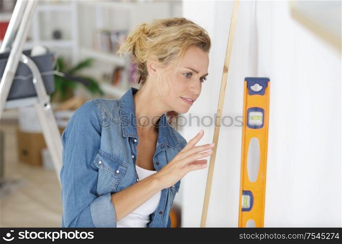 woman measuring a wall with spirit level in room