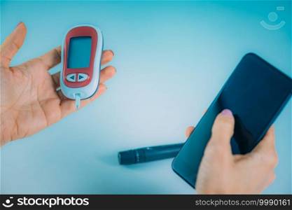 Woman Measuring Blood Glucose Levels, Using Smart Phone to Follow Results. Woman Measuring Glucose Levels, Entering Data into Smart Phone