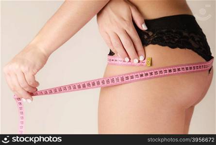 Woman measuring her hips closeup. Woman fit girl in black lingerie measuring her hips with measure tape closeup. Part of female body.
