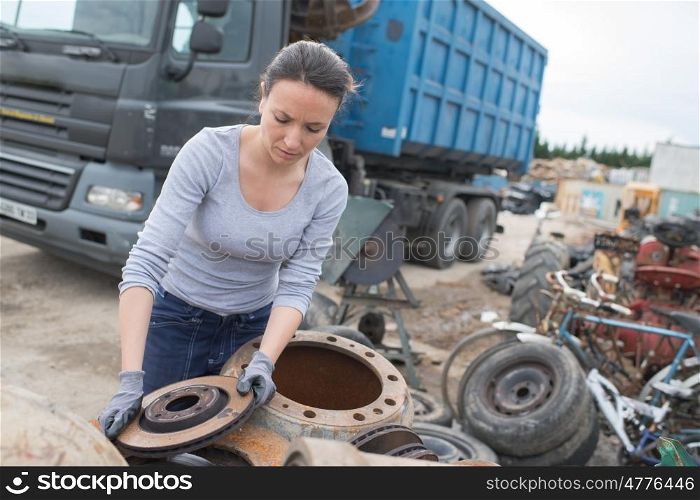 woman mechanic picking axle in car scrap yard