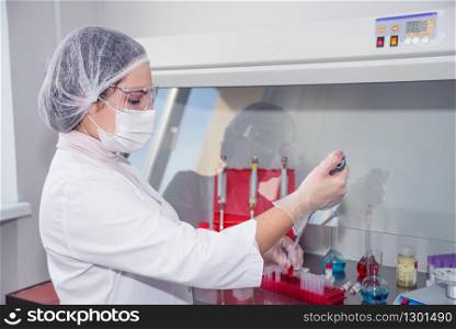 Woman medic in a white protective clothing conducts research in a lab
