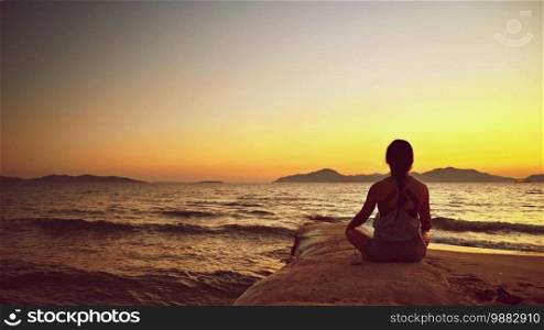 Woman meditates - relaxes at sunset by the sea on the beach. Concept for yoga, health and spa.
