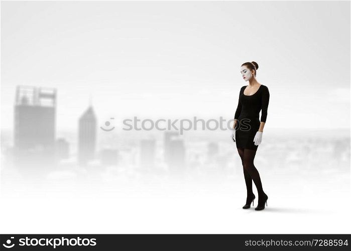 Woman mime in black suit standing against cityscape background. Mixed media. Young woman mime. Mixed media