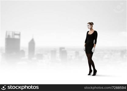Woman mime in black suit standing against cityscape background. Mixed media. Young woman mime. Mixed media