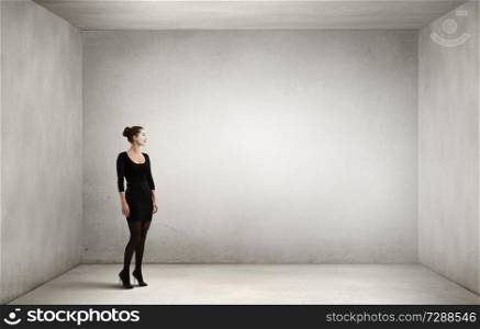 Woman mime in black suit standing in empty room. Mixed media. Young woman mime. Mixed media