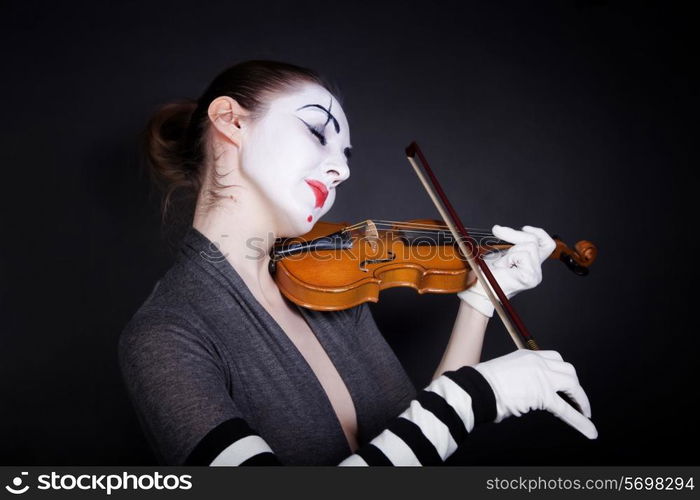 Woman mime in white gloves who plays the violin on a black background