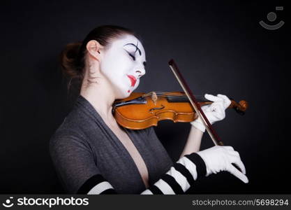 Woman mime in white gloves who plays the violin on a black background