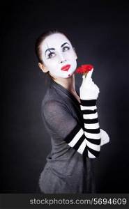 woman mime with theatrical makeup and red flower in hands on black background