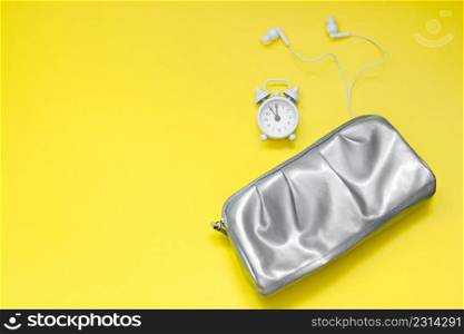Woman modern morning concept. Silver cosmetic bag, alarm clock and headphones on yellow background. Colors of the year 2021 - ultimate gray and illuminating.. Woman modern morning concept. Silver cosmetic bag, alarm clock and headphones on yellow background. Colors of year 2021 - ultimate gray and illuminating.