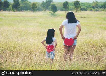woman mother and daughter white tshirt standing on grassland and holding a red heart her back