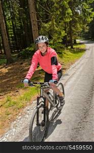 Woman mountain biking in sunny forest cycling path smiling