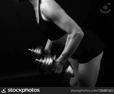woman of Caucasian appearance holds steel type-setting dumbbells in her hands, sports training, dark background, black and white tinting
