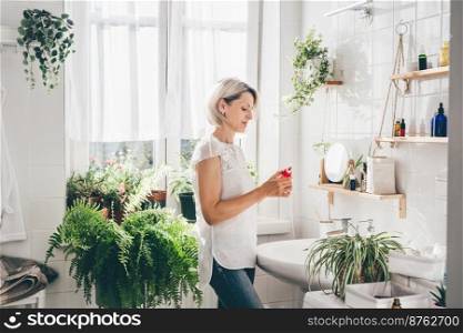 Woman of middle-aged staying in eco friendly white bathroom. Wooden shelves with cosmetics and toiletries against white tile wall. Minimalistic design. Wellness. Comfort home zone. Woman staying in eco friendly white bathroom