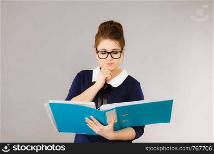 Woman office worker agent holding blue file folder in hands. Young elegant businesswoman or secretary with documents bills. Thinking face expression. Business and paperwork on grey. woman thinking holds file folder with documents