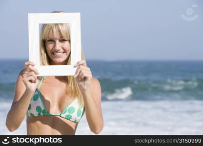 Woman on a beach holding a frame to her face