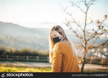 Woman on a yellow coat sitting on a bench with a face mask.