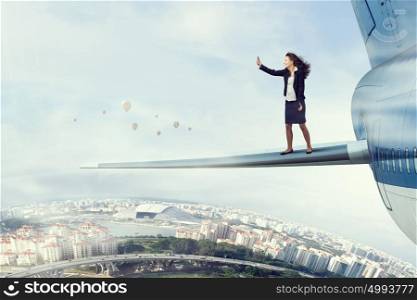 Woman on airplane wing high in sky. Businesswoman standing on airplane wing and making selfie