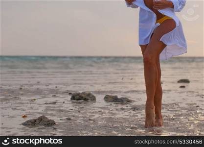 Woman on beach at sunset. Woman in bikini and white shirt walking on beach at sunset