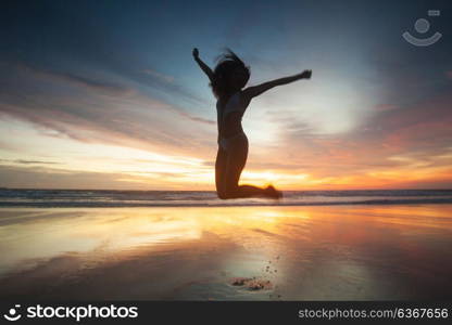 Woman on beach at sunset. Woman in bikini jumping with rised hands on the beach at sunset. Bali island, Indonesia