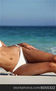 Woman on beach. Woman with perfect body in bikini lying on beach over blue sea background