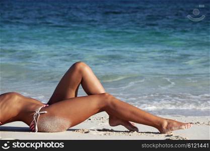 Woman on beach. Woman with perfect body in bikini lying on beach over blue sea background