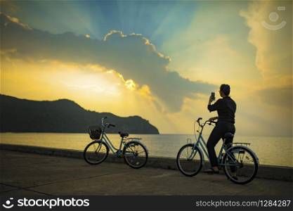 woman on bicycle taking a photograph of amazing sun light sky