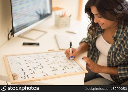 Woman on computer desk wrinting on calendar