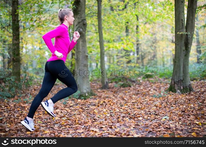Woman On Early Morning Autumn Run Through Woodland Keeping Fit Through Exercise