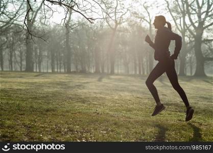 Woman On Early Morning Winter Run In Park Keeping Fit Listening To Music Through Earphones