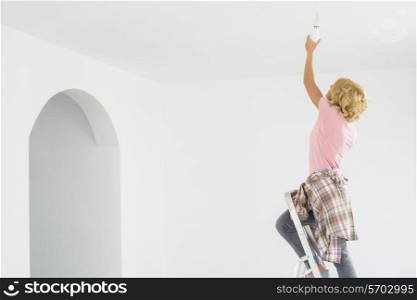 Woman on ladder fitting light bulb in new house