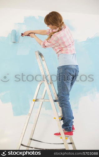 Woman on ladder painting wall with paint roller